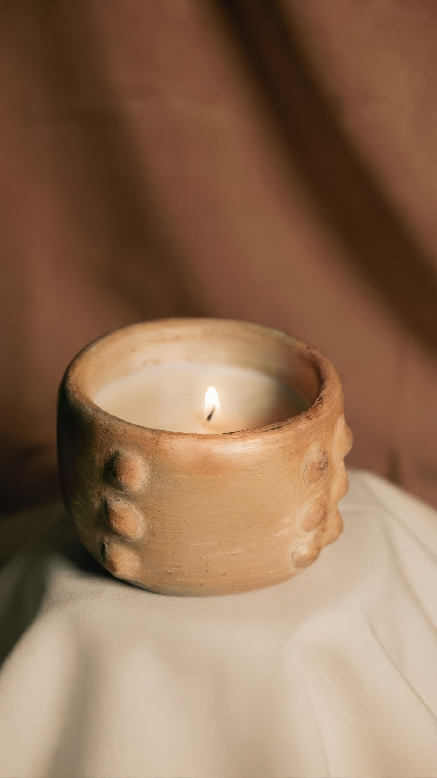 Bougie en poterie de Sejnane, beige, allumée sur un drapé crème